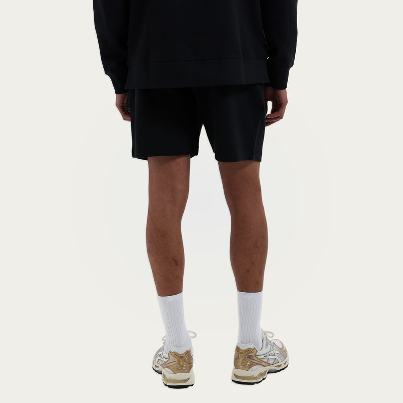Model draagt de Branded Sweater en Branded Shorts in zwart, achteraanzicht
